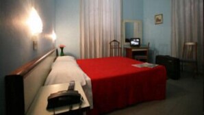 A hotel room with a bed, a desk, a chair, a TV, and a lamp.