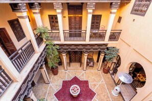 A courtyard with a central fountain, potted plants, and a tiled floor.