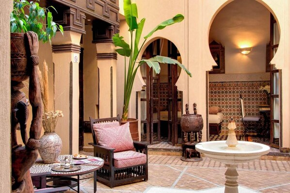 A traditional courtyard with a tiled floor, a wooden chair, a table with a vase, and a fountain.