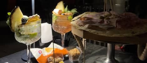 Ein Tisch mit verschiedenen Speisen und Getränken, darunter ein Glas mit Limettenscheibe und Minze, ein Teller mit Brot und Fleisch sowie eine Dessertplatte.