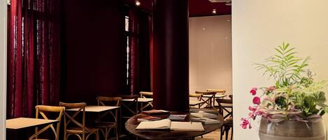 A dimly lit room with wooden chairs and tables, a large pillar, and a potted plant.