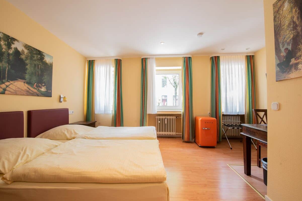 A hotel room with two beds, a radiator, a table, and a chair.