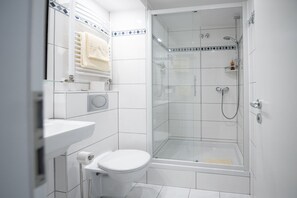 A modern bathroom with a glass-enclosed shower, a white toilet, and a sink with a towel rack.