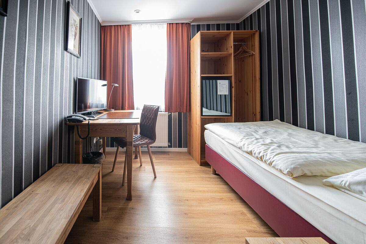 A compact hotel room with a bed, a desk with a chair, a television, and a wardrobe.
