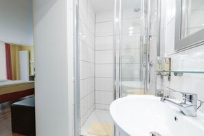 Ein modernes Badezimmer mit einer Duschkabine aus Glas, einem weißen Waschbecken und einem Spiegel.