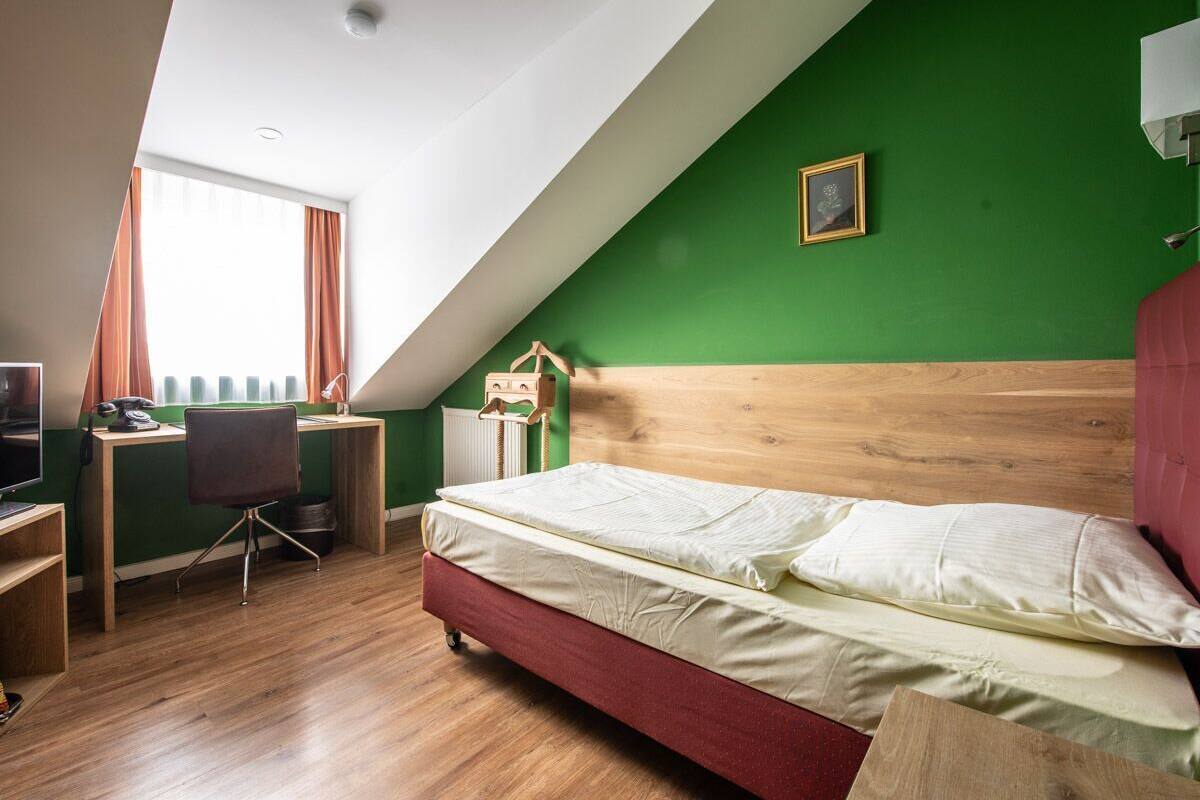 A room with a bed, desk, chair, and a window with curtains.