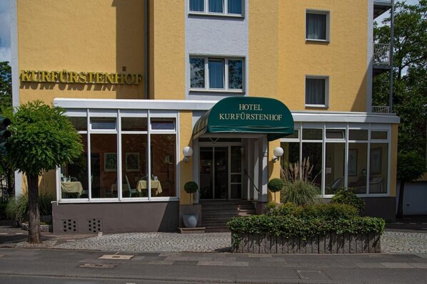 Ein Hotel namens 'Kurfürstenhof' mit einer modernen Fassade, großen Fenstern und einem einladenden Eingang.