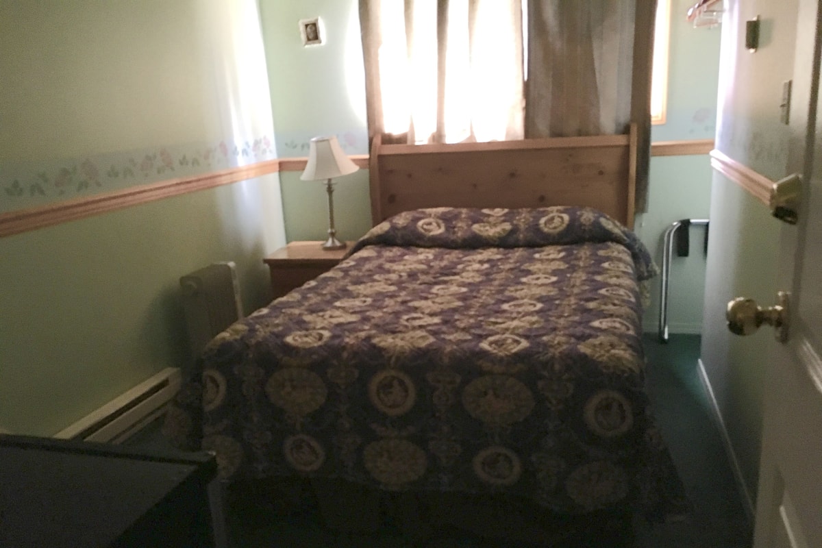 A bedroom with a bed, a nightstand, a lamp, and a door.