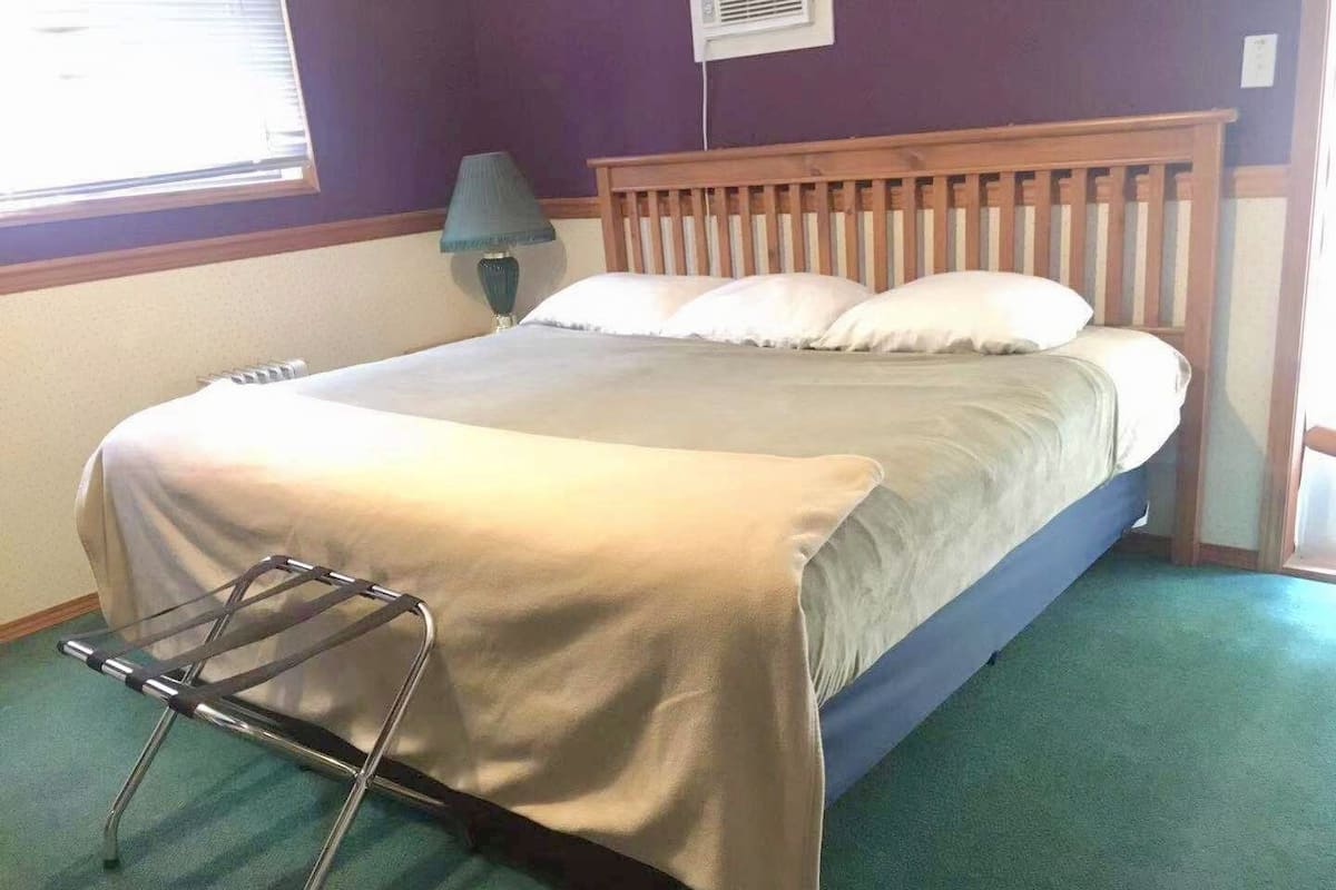 A bedroom with a bed, a nightstand, a lamp, and a window.