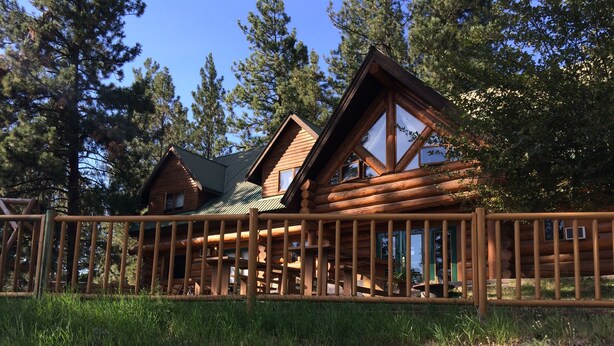 A log cabin with a porch, surrounded by tall trees and a wooden fence. - Rainbow Lake Castle Resort (Princeton)