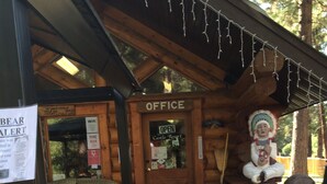 A wooden lodge with a covered entrance labeled "OFFICE," a bear alert sign, and a statue of a Native American figure. - Rainbow Lake Castle Resort (Princeton)