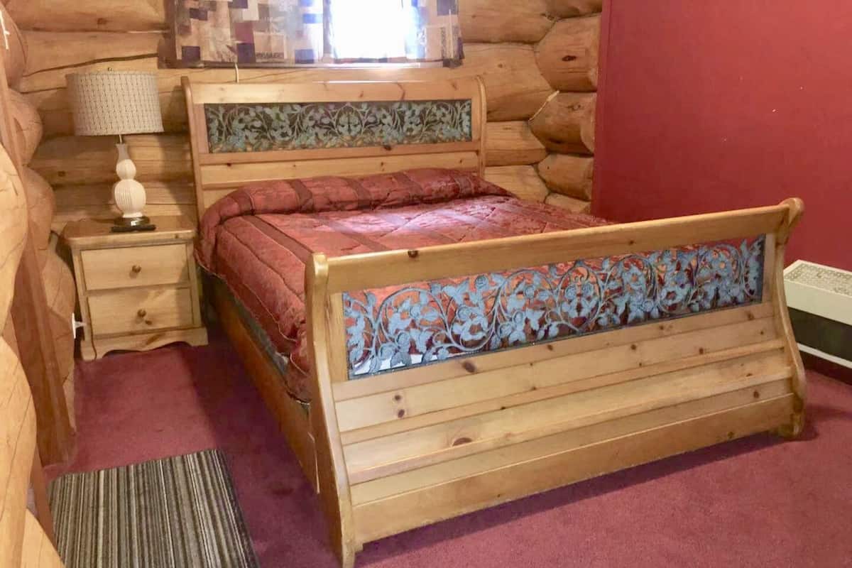 A wooden bed with a floral headboard, a nightstand with a lamp, and a red carpeted floor.