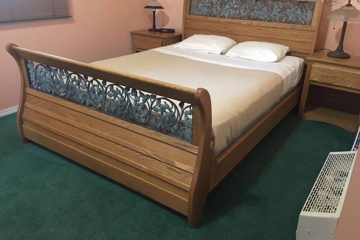 A wooden bed with a decorative headboard, a bedside table with a lamp, and a wall-mounted heater.