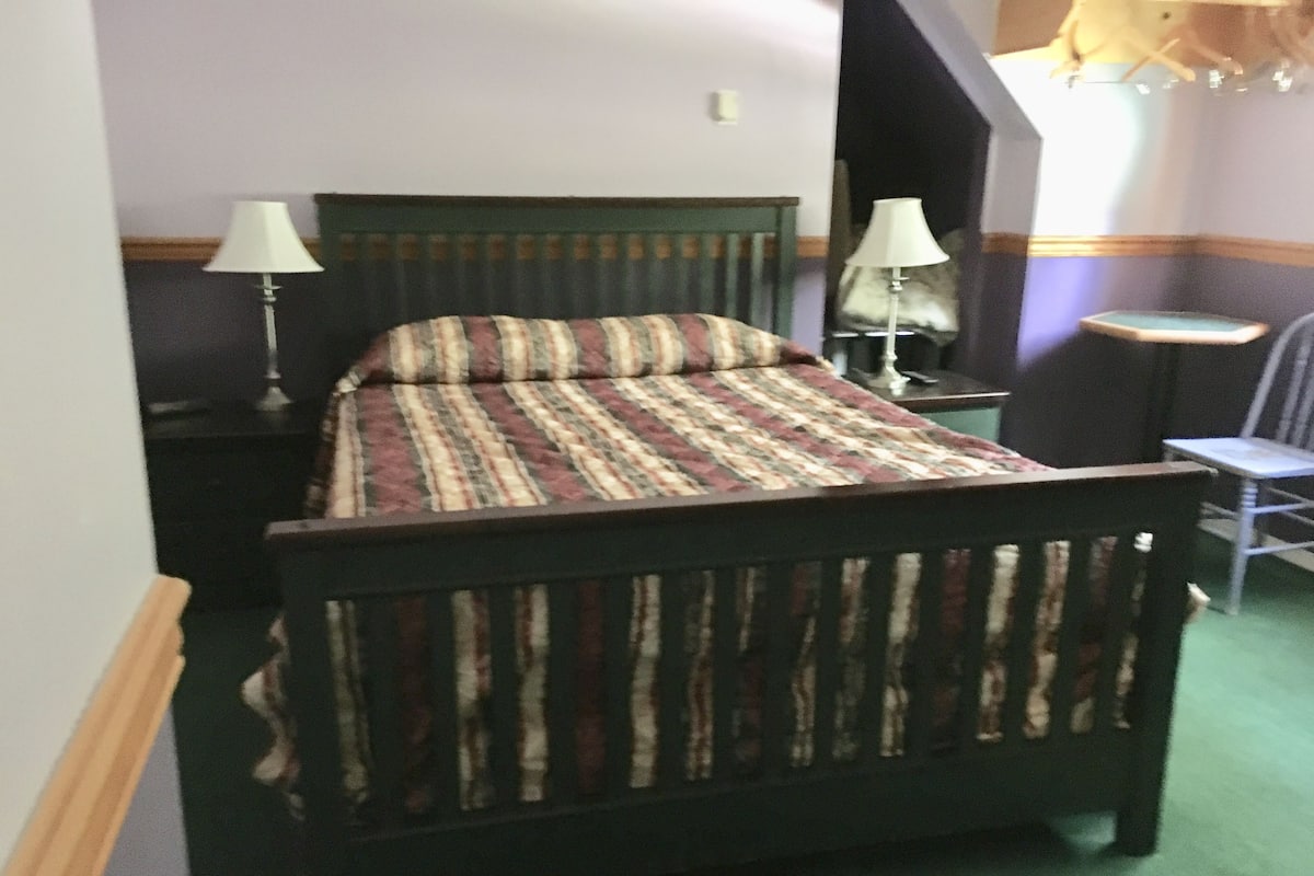 A bed with a striped bedspread, two bedside lamps, a chair, and a small table.