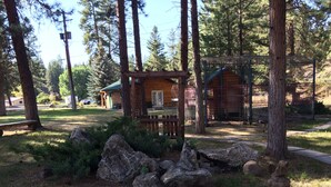 A rustic cabin with a wooden deck, surrounded by a fenced area with a rock garden and a statue. - Rainbow Lake Castle Resort (Princeton)