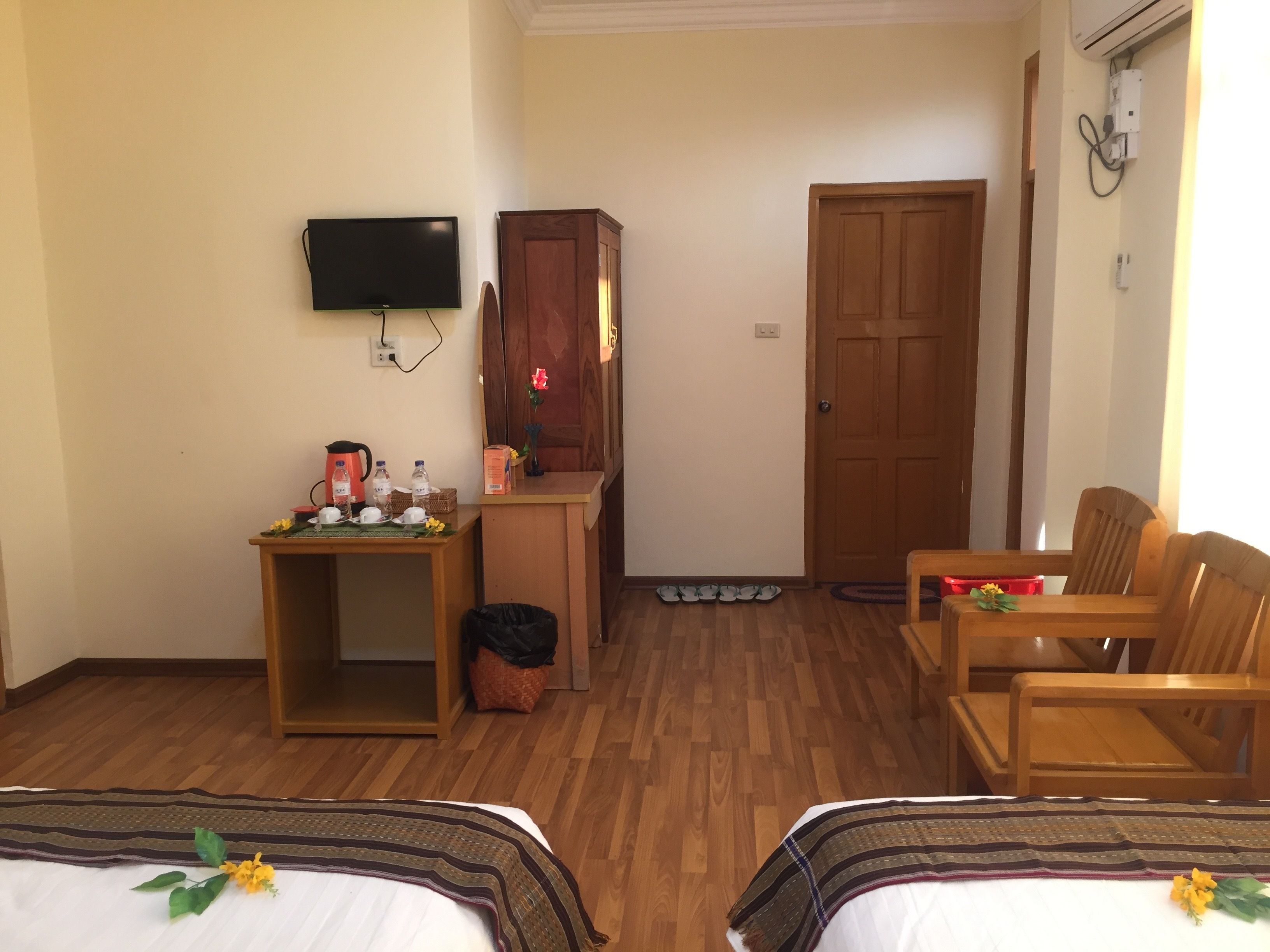 Habitación de hotel con dos camas, un escritorio con televisor, un armario, una puerta y un zapatero.