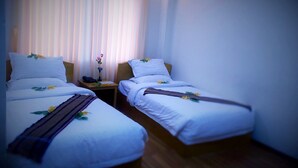 A hotel room with two single beds, a bedside table with a lamp, and a window with vertical blinds.