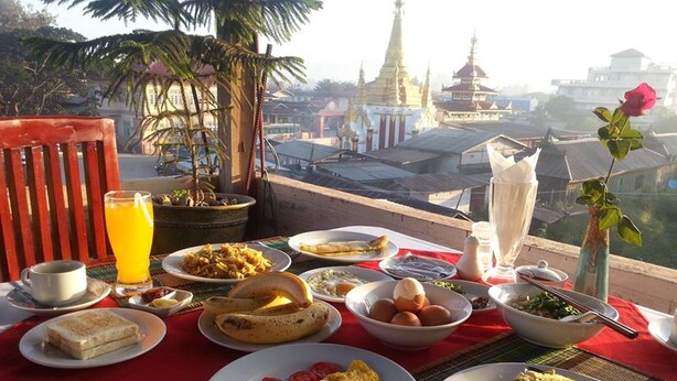 A breakfast table with various dishes, a potted plant, and a view of a temple in the background.