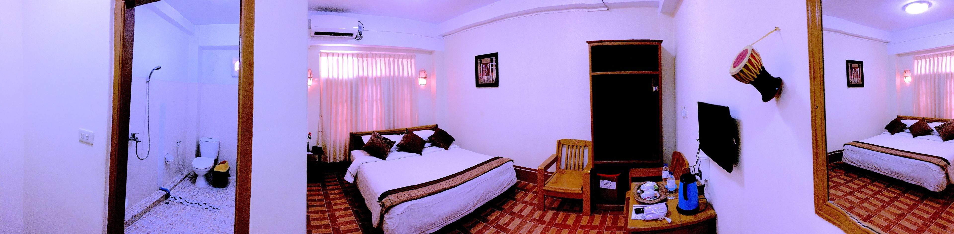 A hotel room with a bed, a chair, a table with a kettle, and a TV.