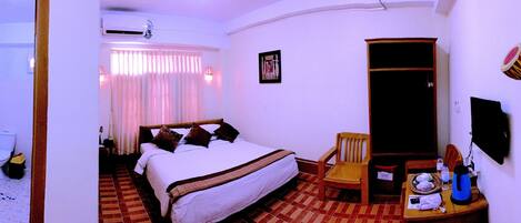 A hotel room with a bed, a chair, a table with a kettle, and a TV.
