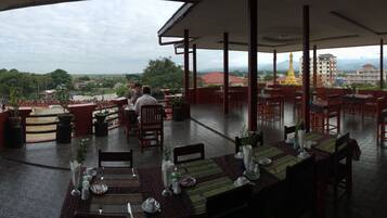 A restaurant with tables set for dining, a view of a river with boats, and a distant view of a golden temple and buildings.