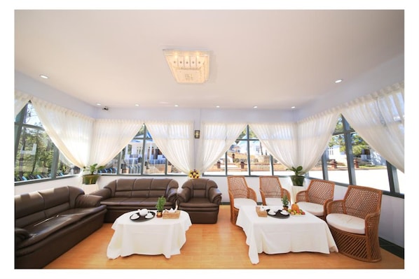A spacious room with a large sofa, two dining tables, and wicker chairs.