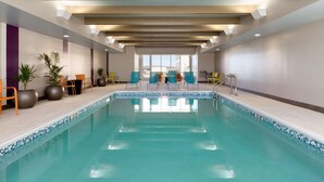 A modern indoor pool with clear blue water, surrounded by lounge chairs and potted plants. - Home2 Suites by Hilton Gillette (Gillette)