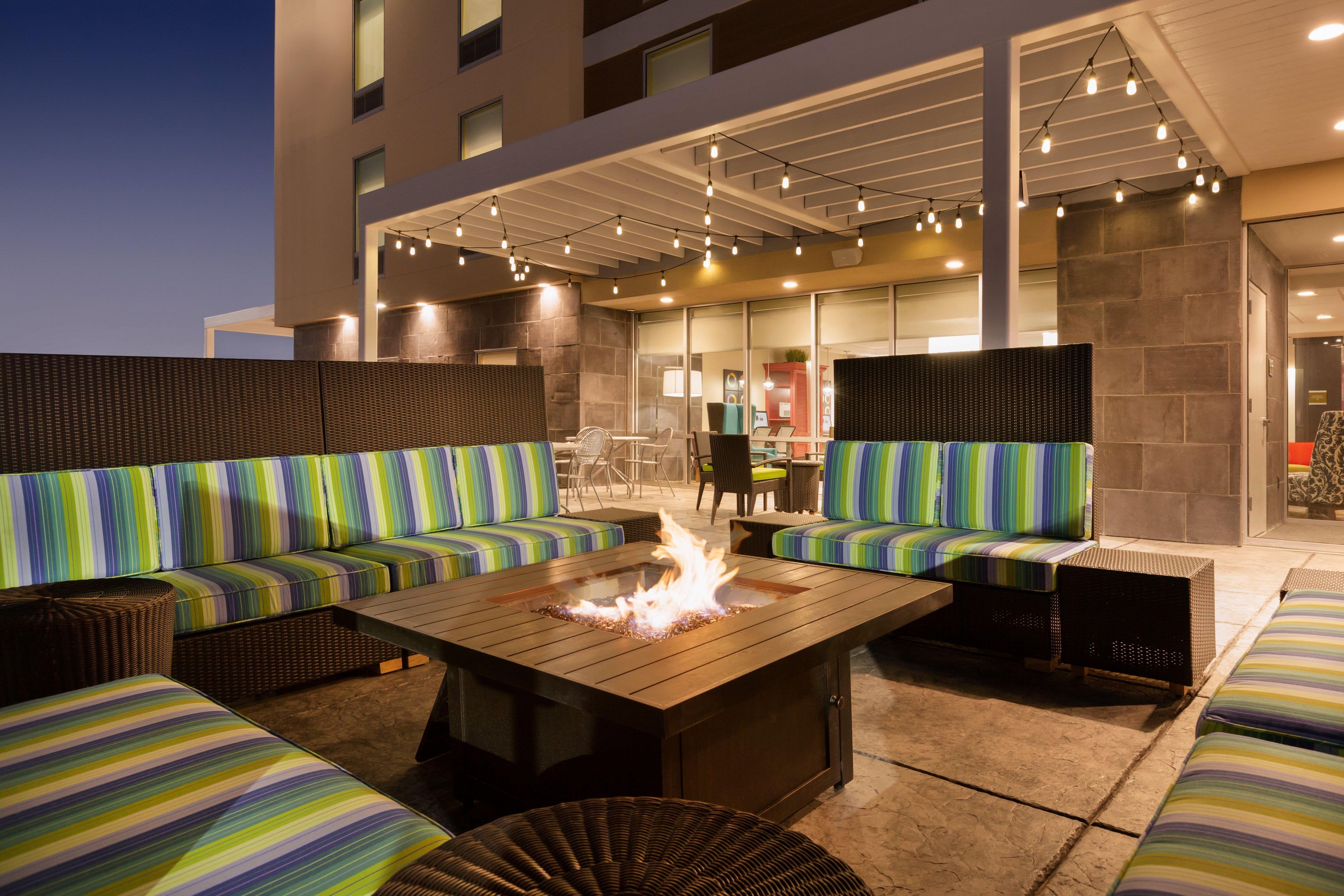 An outdoor seating area with a fire feature, cushioned seating, and a modern building in the background.