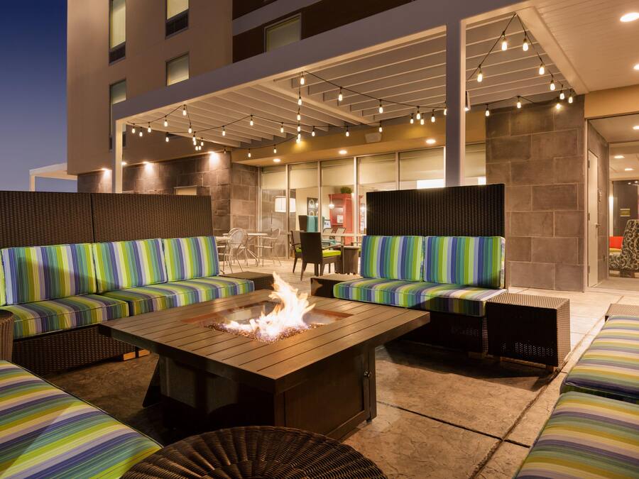 An outdoor seating area with a fire feature, cushioned seating, and a modern building in the background.