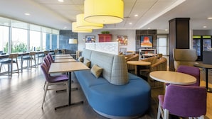 A modern restaurant with a blue booth seating area, wooden tables, and yellow pendant lights. - Home2 Suites by Hilton Gillette (Gillette)