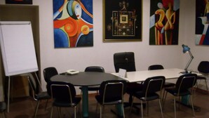 A conference room with a whiteboard, a table, and six chairs. There are abstract paintings on the walls.