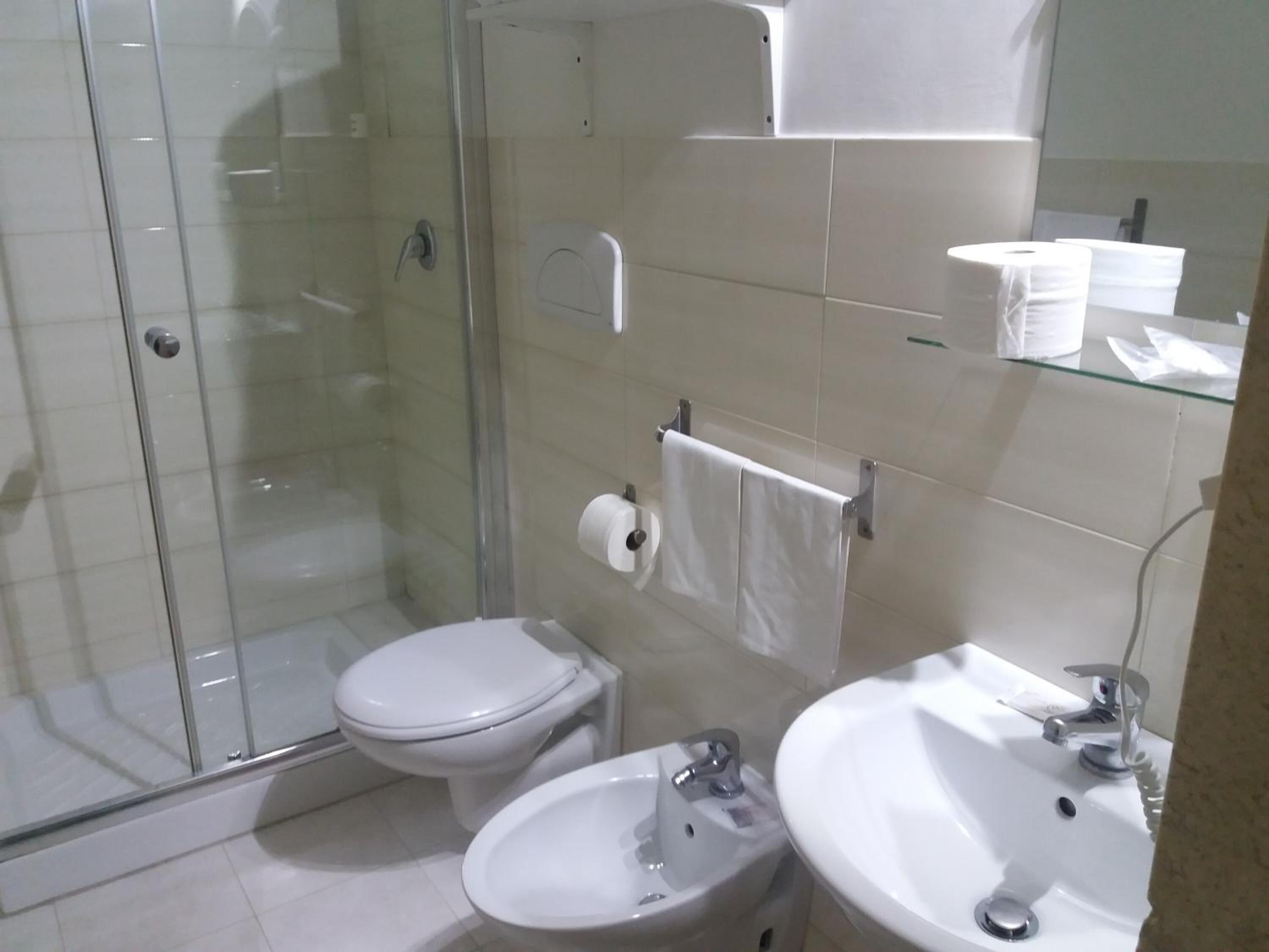 Bagno con doccia vetro, water, lavandino e specchio.