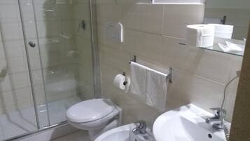 Bagno con doccia vetro, water, lavandino e specchio.