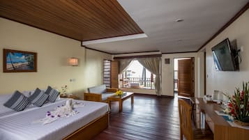 Habitación de hotel con cama, escritorio, silla, mesa, televisor y balcón con vistas.