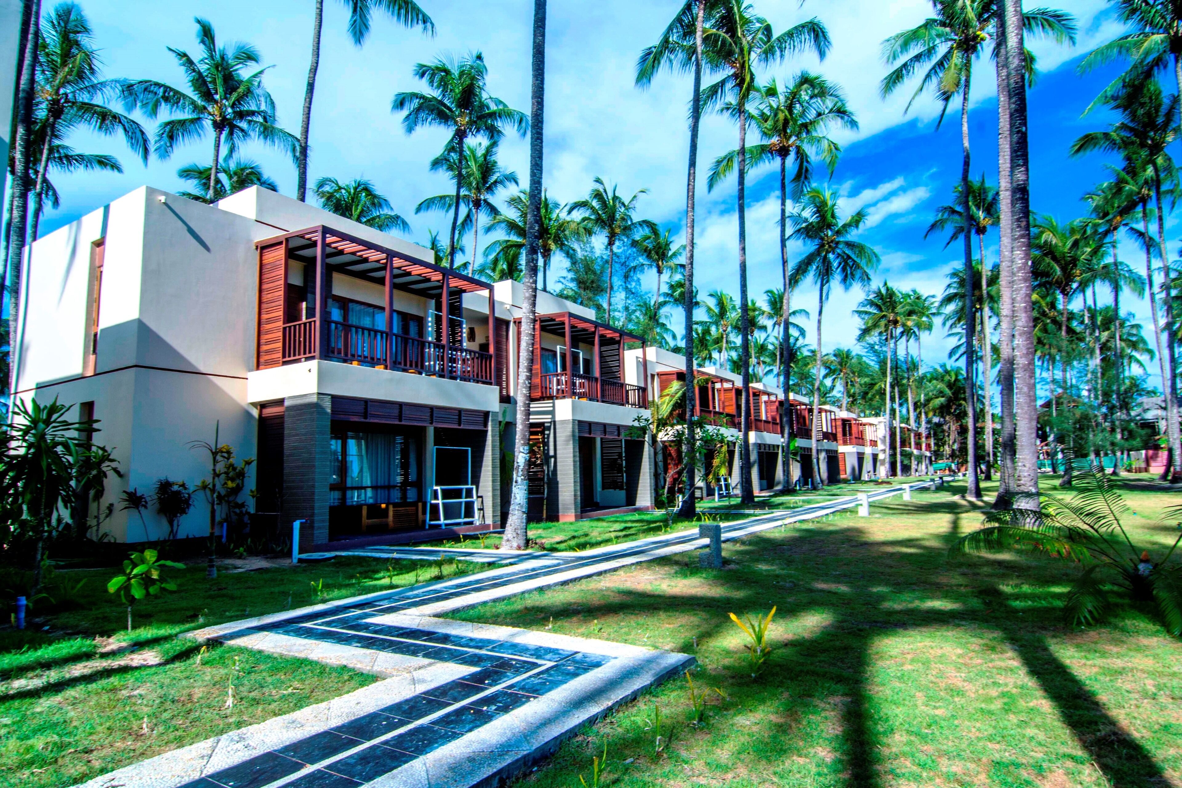 A resort with multiple-story buildings, palm trees, and a well-maintained lawn.