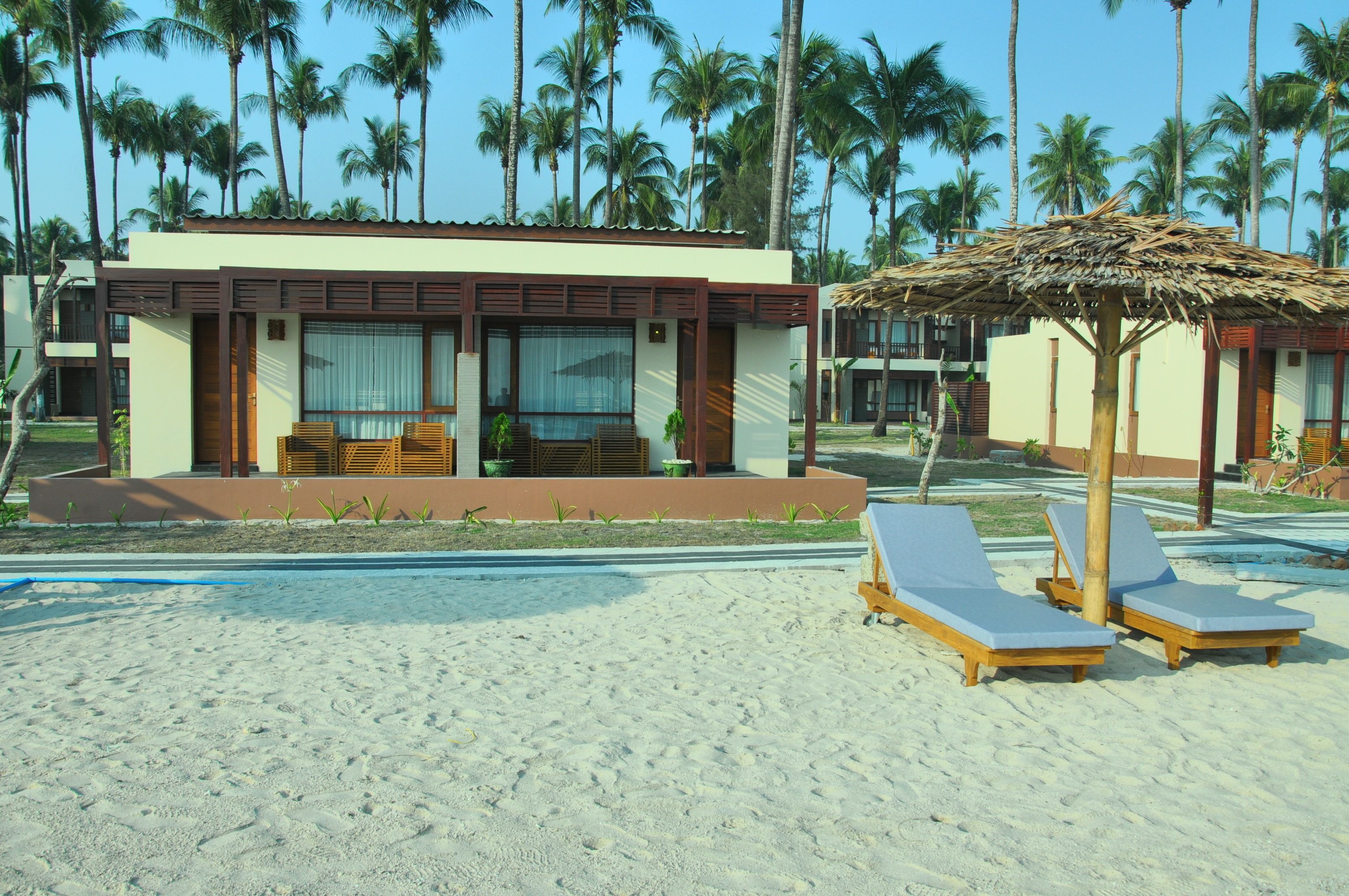 A beachfront hotel with a pool, lounge chairs, and palm trees.