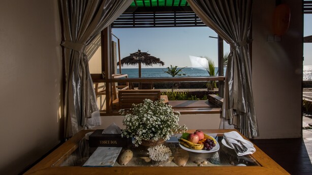 Una habitación con vista al océano, una mesa de madera con un frutero, un libro y una planta.