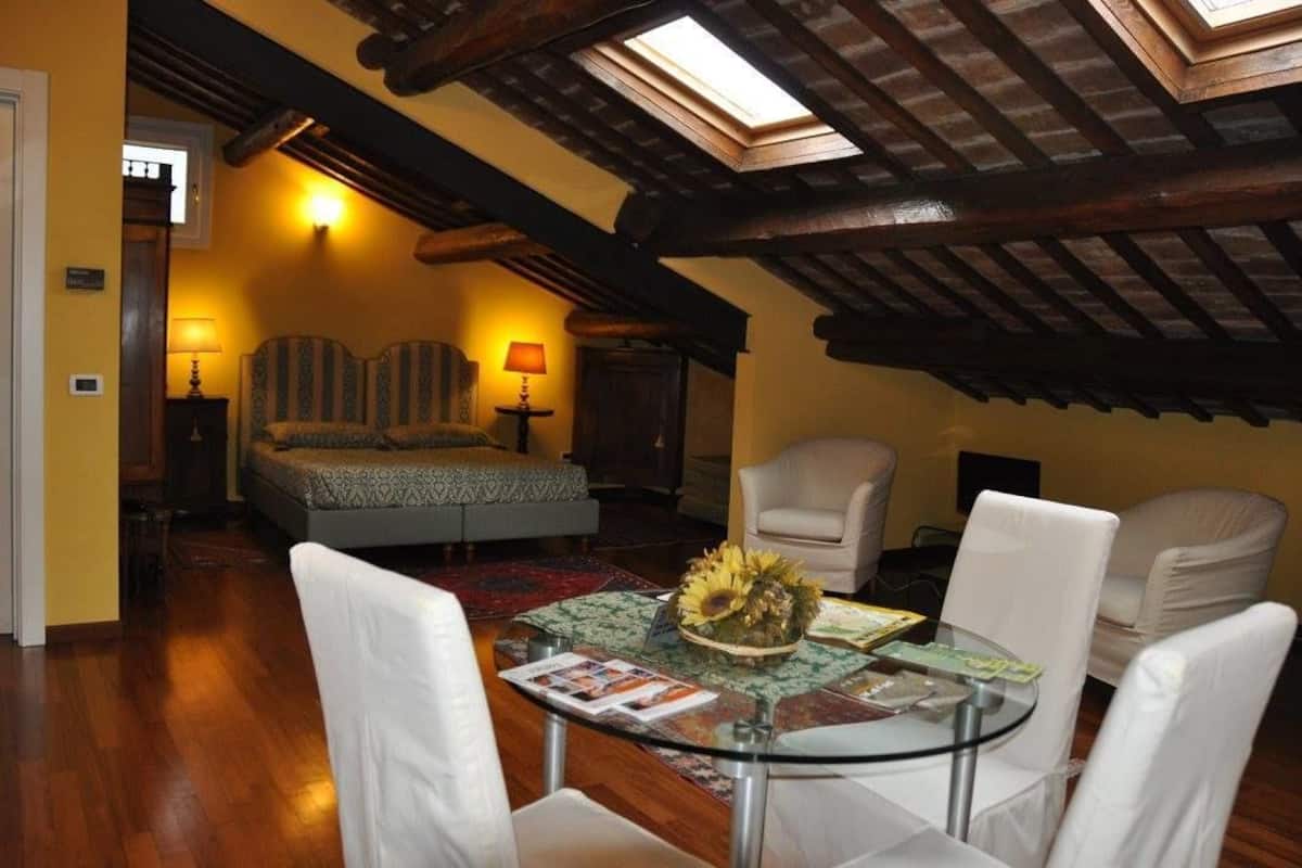 Une pièce confortable avec un lit, deux fauteuils, une table avec un plateau en verre et une lucarne au plafond.