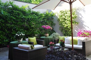 A patio area with wicker furniture, a table with a green tablecloth, and potted plants. - Piazza Nova Guest House (Ferrara)