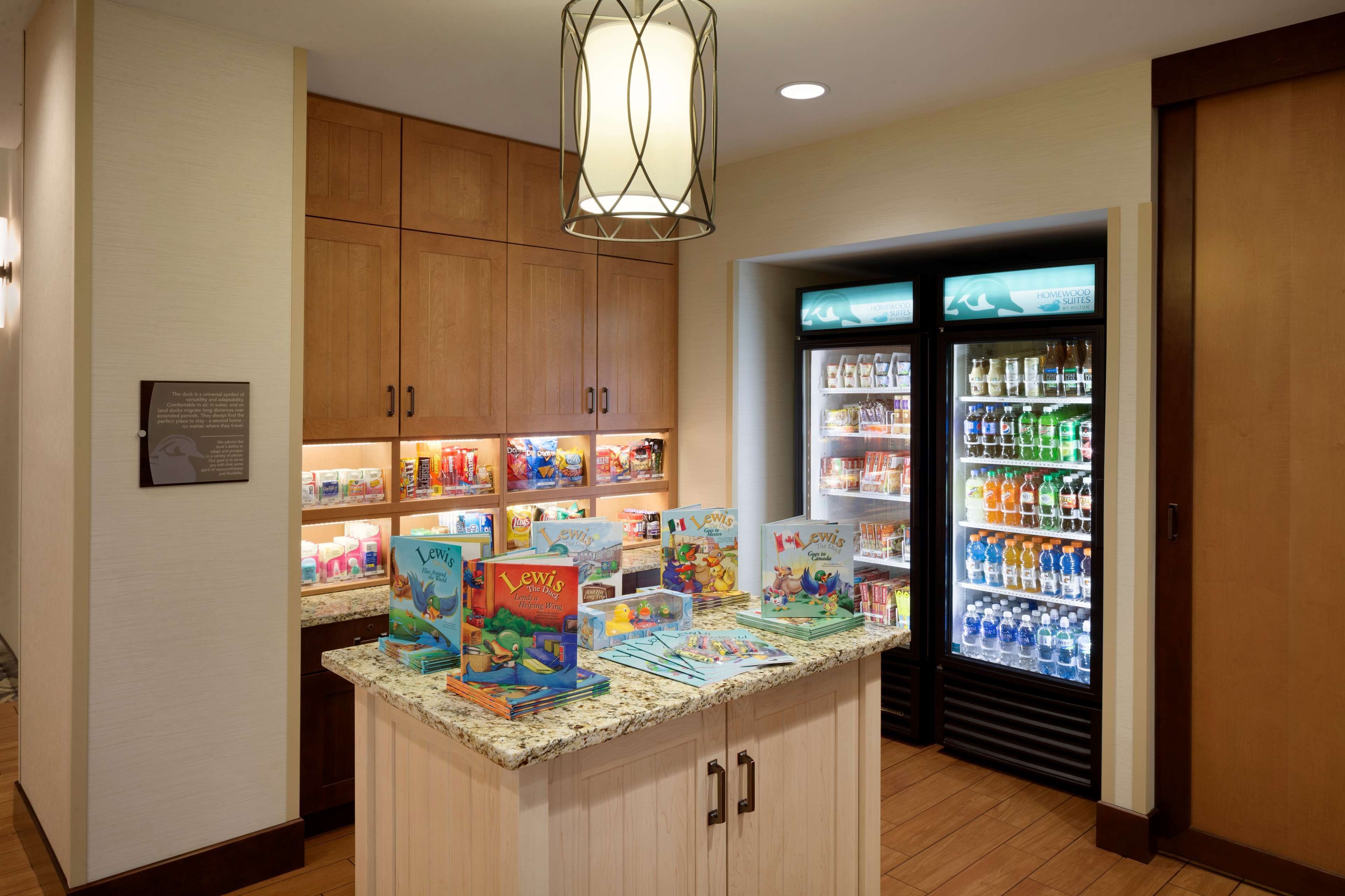 Un vestíbulo de hotel con armarios de madera, una encimera de granito con libros infantiles y un refrigerador lleno de bebidas.