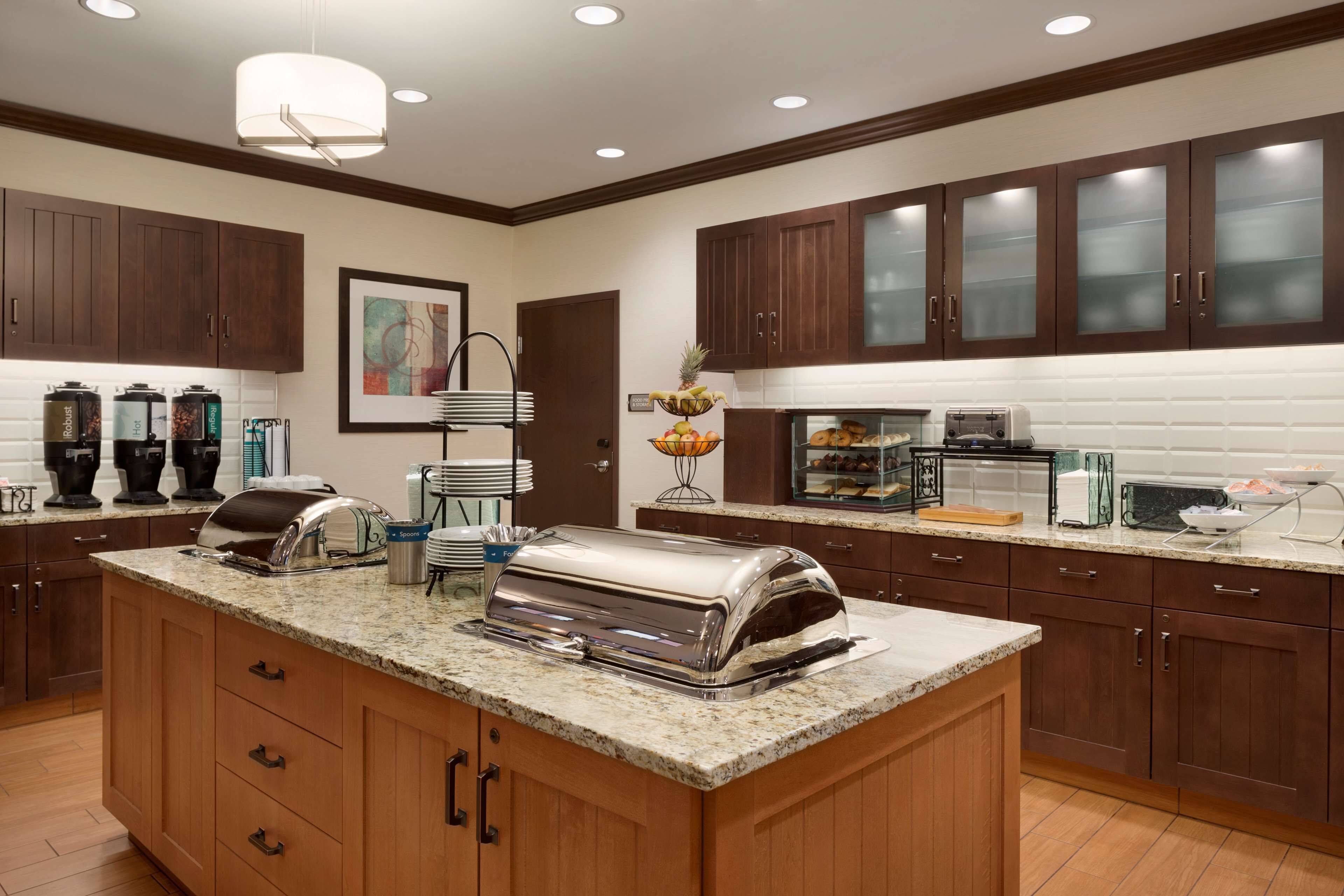 A modern kitchen with wooden cabinets, granite countertops, a built-in island with a toaster, and a coffee station.