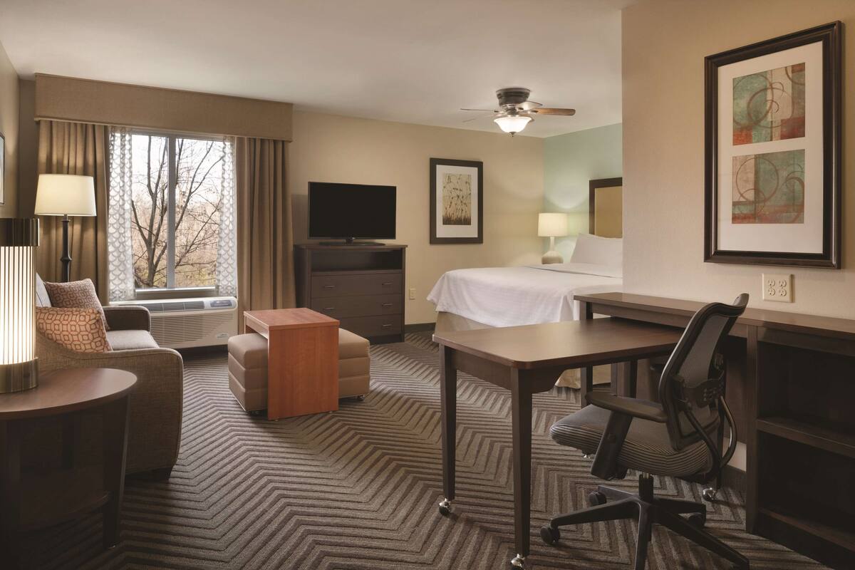 A hotel room with a bed, desk, chair, TV, and a window with curtains.