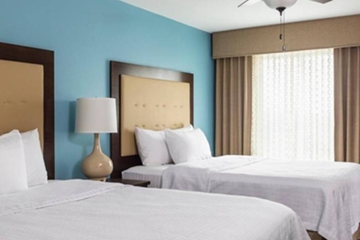Une chambre d’hôtel avec deux lits, un ventilateur de plafond, une lampe et une fenêtre avec des rideaux.