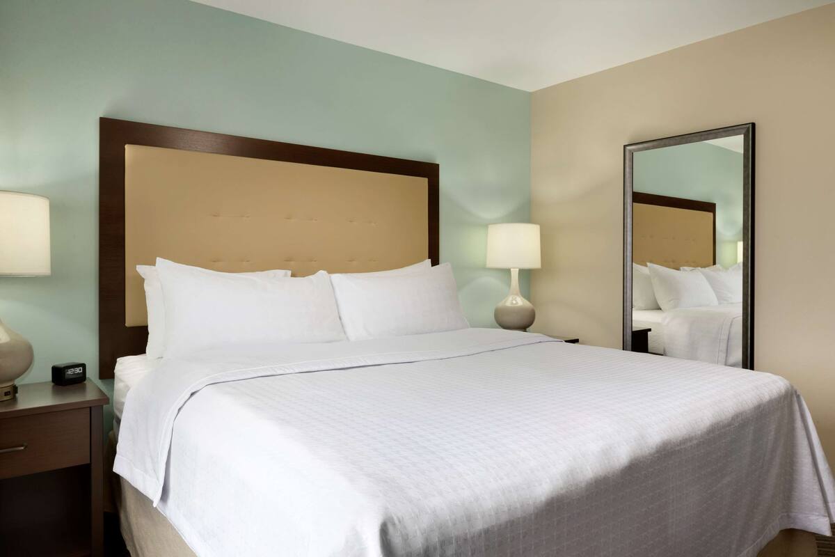 A neatly made bed with white linens, a wooden headboard, and two bedside lamps.