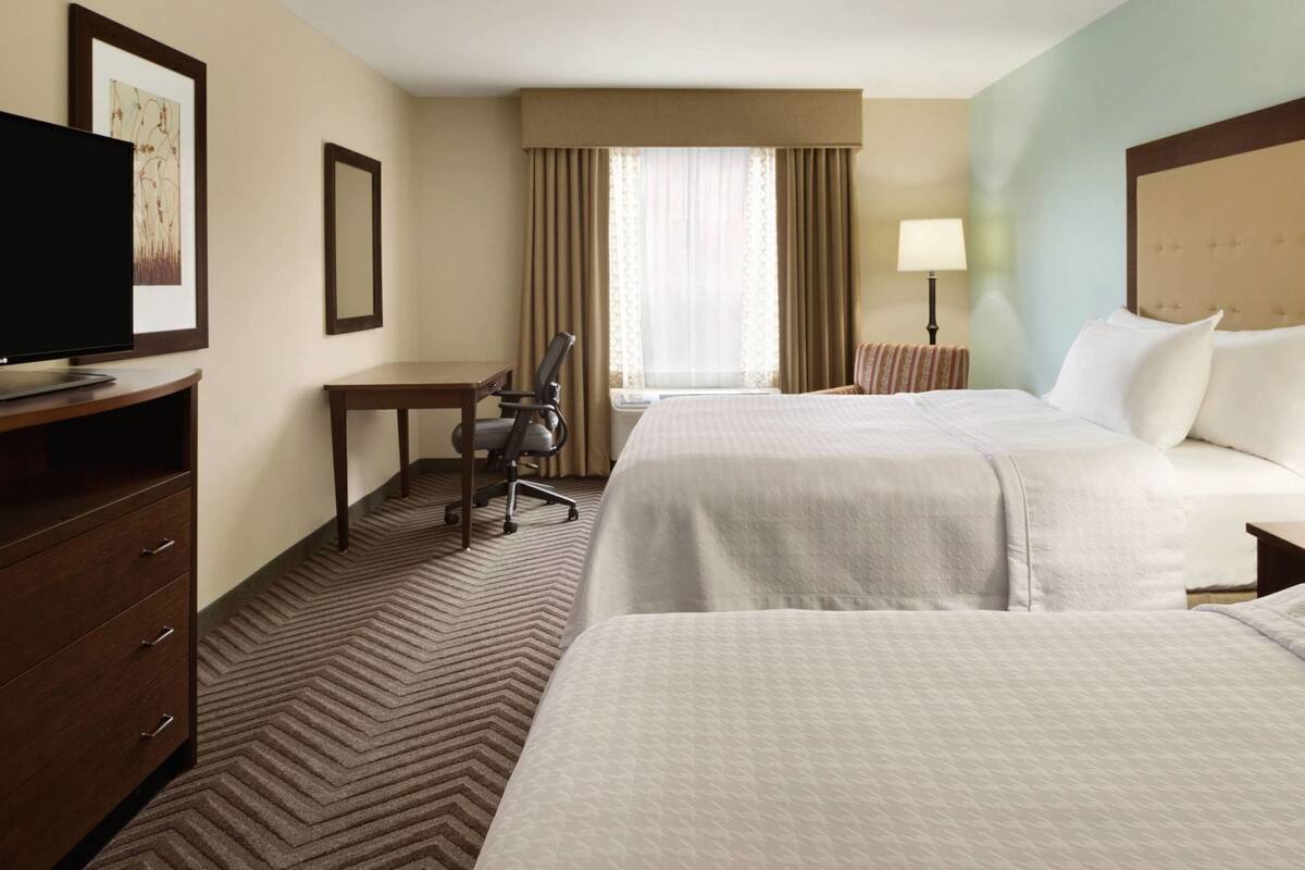 A hotel room with two beds, a desk, a chair, a TV, and a window with curtains.