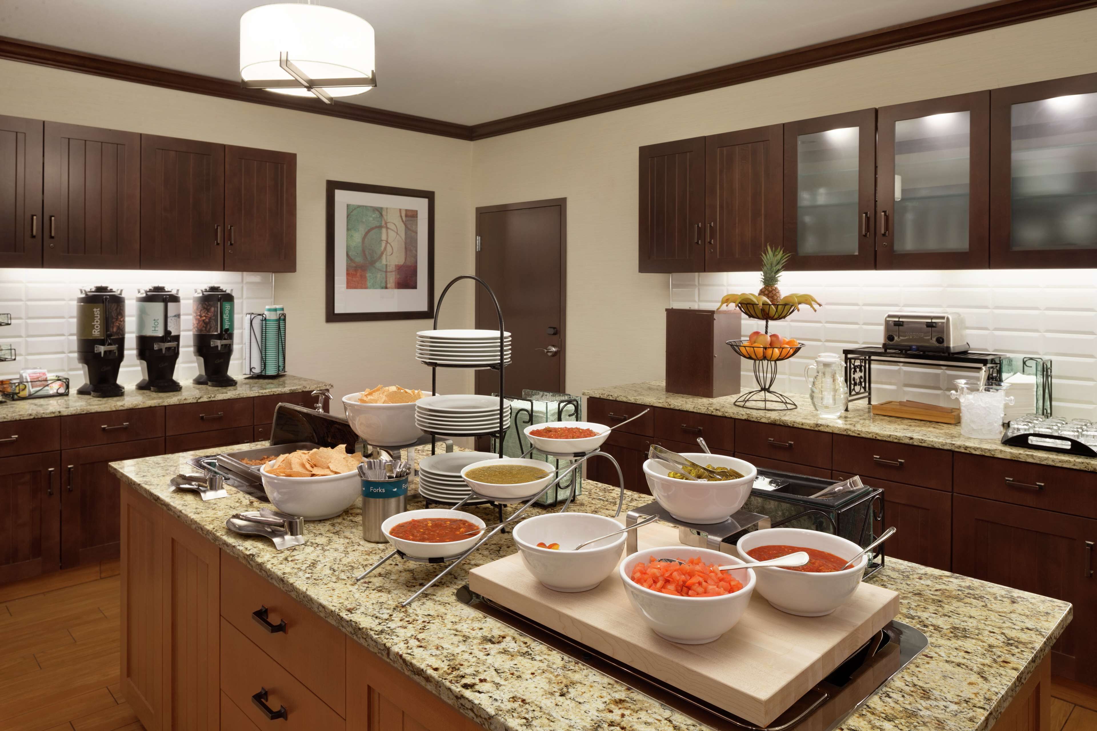 A buffet setup with various food items and serving utensils on a granite countertop.