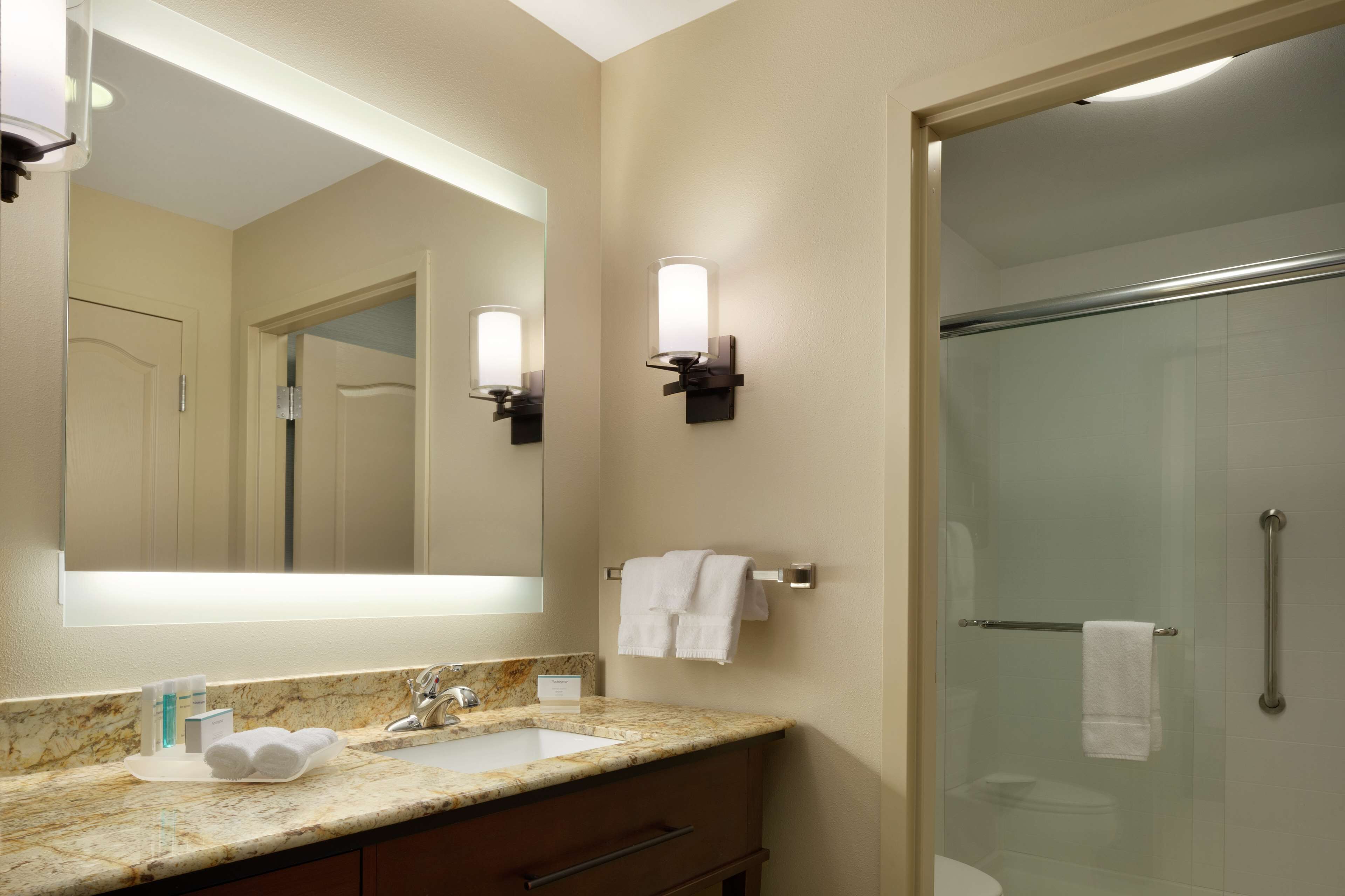 A bathroom with a marble sink, a large mirror, two wall-mounted lights, a glass shower enclosure, and a towel rack.