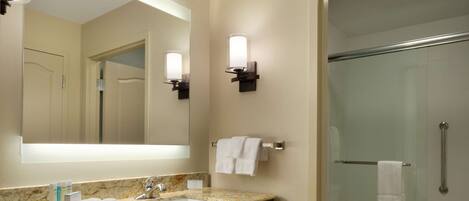 A bathroom with a marble sink, a large mirror, two wall-mounted lights, a glass shower enclosure, and a towel rack.
