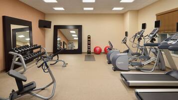 A gym with treadmills, elliptical machines, dumbbells, and exercise balls.