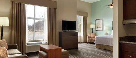 Ein Hotelzimmer mit Bett, Fernseher auf einer Kommode, Schreibtisch, Sessel und einem großen Fenster mit Vorhängen.